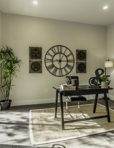 Modern home office with minimalist decor, large wall clock, and glass doors leading outside.