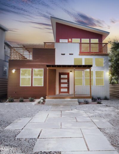 Modern two-story house with a combination of wood and red siding under a twilight sky.