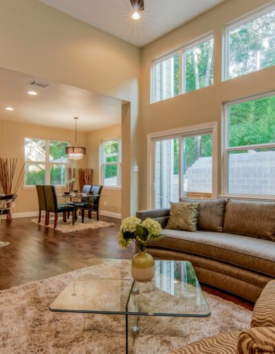 Spacious living room with high ceilings, large windows, and an open-concept kitchen in the background.