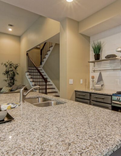 Modern kitchen with stainless steel appliances, granite countertops, and staircase in the background.